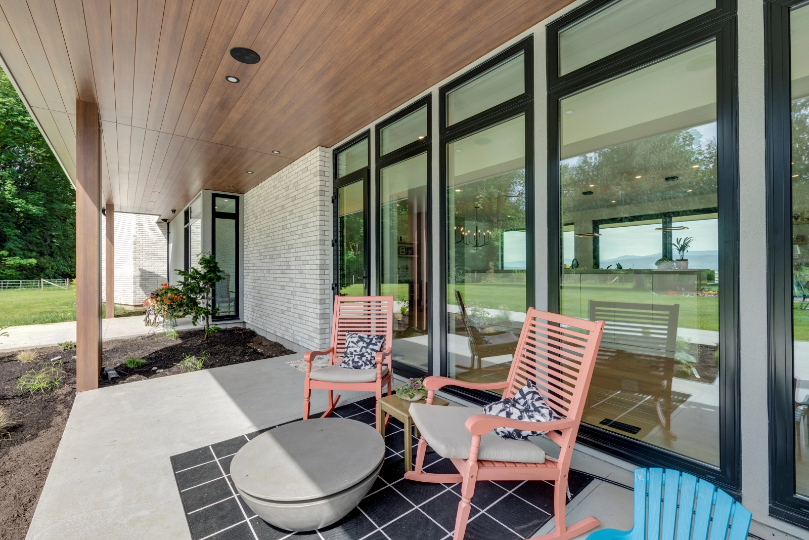 A seating area outside a modern home with black vinyl windows providing a view of the inside.